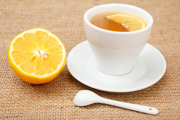 White cup of tea and a piece of lemon on sackcloth background