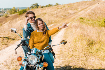 Plakat happy couple sitting on motorbike and girlfriend showing something