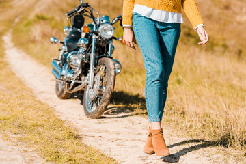Naklejka premium cropped view of young woman walking along trail near retro motorbike