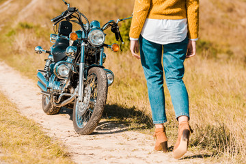 cropped view of young woman walking along trail near vintage motorbike
