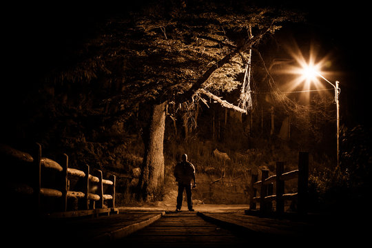 Night stalker concept. Man standing on wood bridge under street light in dark night