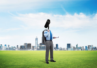 Camera headed man standing on green grass against modern cityscape