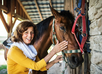 A senior woman with a horse standing by a stable.