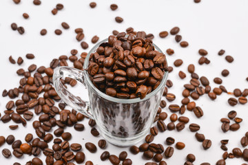 Grains of coffee are poured into a glass cup on a white background