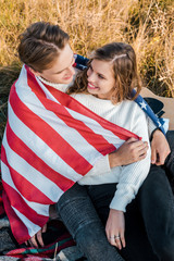 smiling couple with american flag at picnic, independence day concept