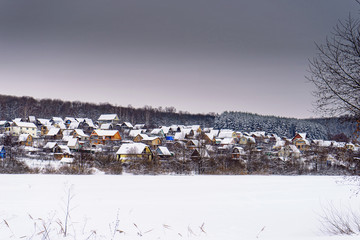 Winter landscape with cottage village on a hill near the forest