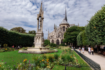 Fototapeta na wymiar Paris, France - August 13, 2017. Medieval Notre Dame de Paris, most visited french monument of Gothic architecture. View from Square Jean XXIII - park with Virgin Fountain and flowers near Cathedral.
