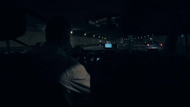 Moody and atmospheric, night dark shot of taxi driver driving cab through tunnel, with gps navigation system on and taximeter measuring kilometers and fare, on way from airport to city