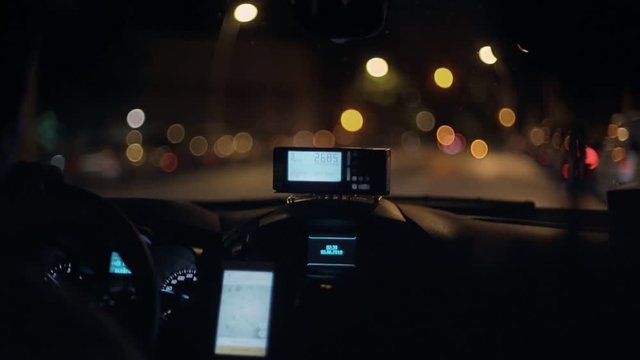 Closeup slowmotion shot of taximeter screen technology counting kilometers and fare due to be paid, installed in taxi driving through midnight city, traffic free streets