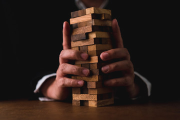business man try to build wood block on wooden table and black background business organization startup concept