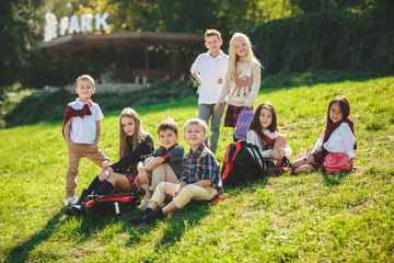 A group of happy smiling children of school and preschool age are sitting on the green grass in the park. The childhood, Kids fashion, school, education, friends, lifestyle, leisure, schoolchildren