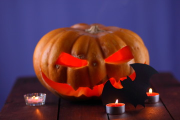 Halloween pumpkin. Candles, bat and glowing pumpkin. Harvest for Halloween. Dark atmosphere for holiday. Bat and light of candles. Pumpkin on wooden boards