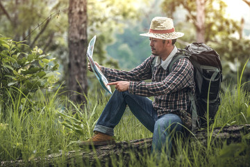 hiker man with backpack sitting and look at map and checking in the forest