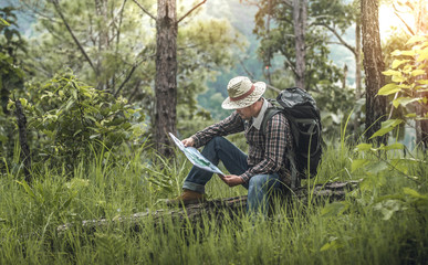 male hiker with backpack sitting and look at map and checking in the forest