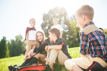 A group of happy smiling children of school and preschool age are sitting on the green grass in the park. The childhood, Kids fashion, school, education, friends, lifestyle, leisure, schoolchildren