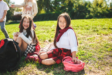 A group of happy smiling children of school and preschool age are sitting on the green grass in the park. The childhood, Kids fashion, school, education, friends, lifestyle, leisure, schoolchildren