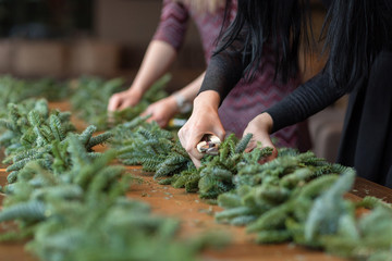 Florist at work: woman hands making christmas decorations garland of fir. Happy new year dinner feast