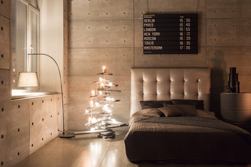 Modern empty bedroom in loft style with grey colors and wooden hand made Christmas tree with presents. warm and cozy evening