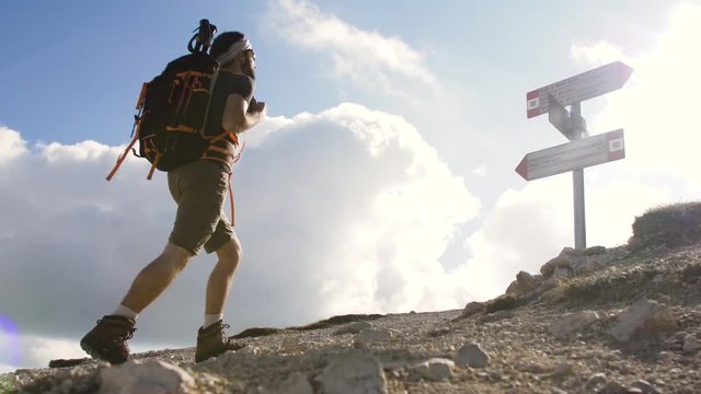 Trekker at mountain crossroad with signs walking up with backpack, boots and trekking poles. Clouds moving on the background. Abruzzo Italy.