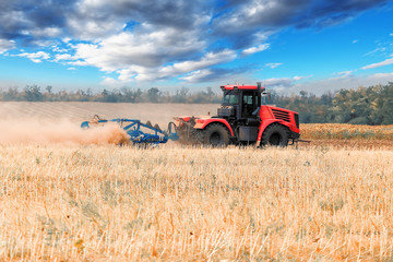 Obraz premium Red tractor plowing field, raising clouds of dust