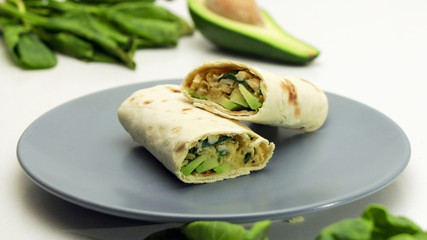 Healthy lunch snack. Tortilla wraps with Avocado, Spinach, Cheese and Bell Pepper on a Grey Plate on a White Background