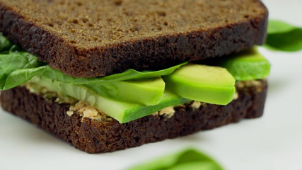 Fototapeta na wymiar Avocado sandwich on dark rye bread made with fresh sliced avocado, spinach and cream cheese