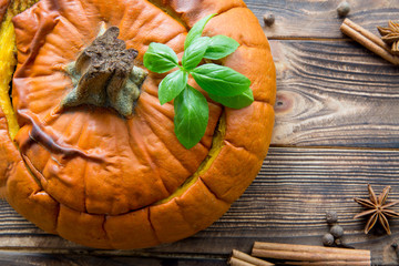 Baked meal in pumpkin on rustic brown wooden background. Stewed potatoes with carrot and roasted meat (veal and pork), decorated with basil leaves. Autumn mood, thanksgiving fall background.