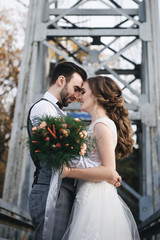 Happy young smiling bride and groom are standing on the suspension bridge. Wedding photos in an interesting place
