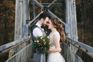 Happy young smiling bride and groom are standing on the suspension bridge. Wedding photos in an interesting place