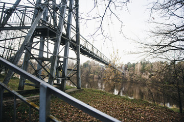 Metal suspension pedestrian bridge across the river. Beautiful view of the bridge, river and forest. Autumn nature
