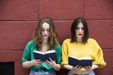Two lovely hipster woman are standing against a red wall with books in their hands. Fashion conception. 