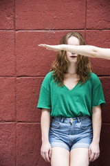 Woman sitting in front of a red wall her eyes covering and blinded by a woman's arm. Emotions...