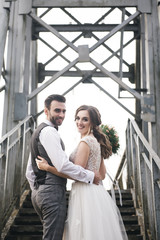 Fototapeta premium Happy young smiling bride and groom are standing on the suspension bridge. Wedding photos in an interesting place