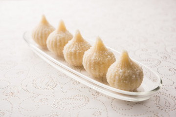 Sweet Modak made using coconut, khoya and sugar. Popular Maharashtrian recipe offered to lord Ganesha in Ganesh Festival. Served in a plate. Selective focus