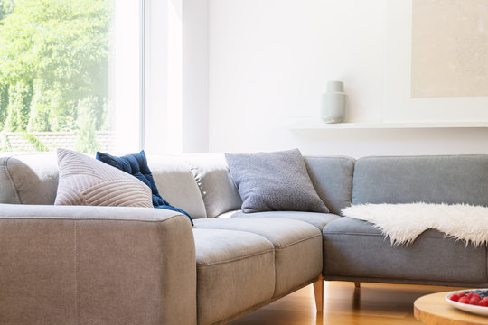 Pillows on grey corner couch in scandinavian white living room interior with window. Real photo