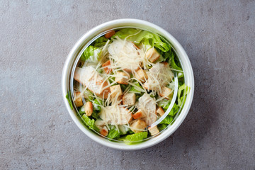 Caesar salad in take away bowl on gray stone background, from above