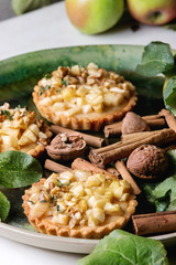 Homemade sweet apple shortbread tartlets in green ceramic plate with cinnamon sticks, walnuts,...