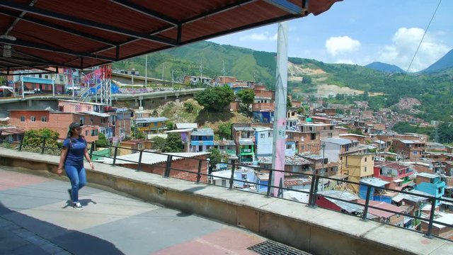 Girl walking on walkway under roof with view of Comuna 13 neighborhood, Medellin Colombia