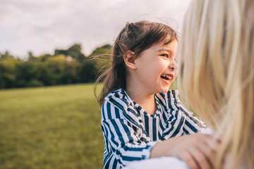 Image of happy cute little girl laughing and playing with her pretty mom in the park. Loving mother and daughter spend time together in the park. Motherhood and childhood. People, family and emotion