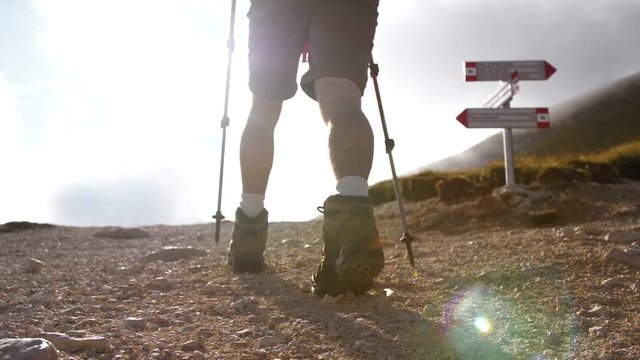 Trekker at mountain crossroad with signs walking up with backpack, boots and trekking poles. Clouds moving on the background. Low angle shot. Abruzzo Italy.