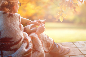 girl is wrapped in a warm cozy blanket sitting on the terrace and drinking coffee tea on an autumn afternoon outdoor lifestyle lagom,hygge