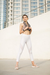 Young pretty woman in sporty top and white leggings holding little towel on shoulders while dreamily looking aside over fuzzy background