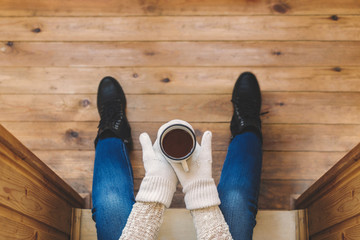 A girl in the boots with an iron mug of coffee on the terrace of a wooden house. Winter concept