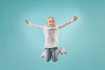 Fototapeta na wymiar Adorable small child at blue studio. The girl is jumping and smiling. Young emotional surprised teen girl. Human emotions, facial expression concept.