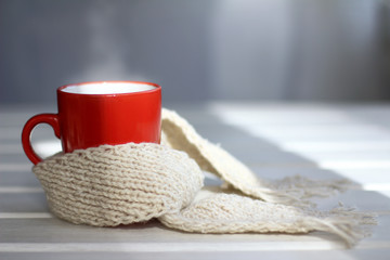 Fototapeta na wymiar cozy home atmosphere warming/ red mug of hot drink in knit scarf on a table