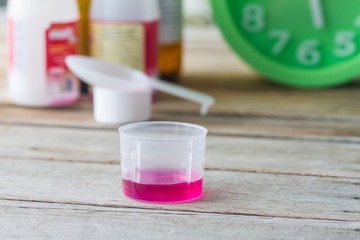 liquid medicine in plastic glass on wooden table.