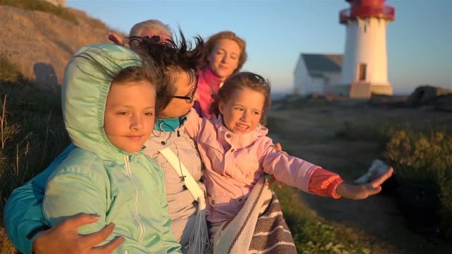 Big happy family admiring the sunset or sunrise on the rocky North shore of the sea with an old lighthouse