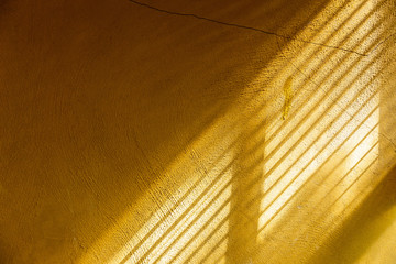 Yellow cement wall touching sunlight through window to show surface of rough wall and making separating parts of light and shadow.