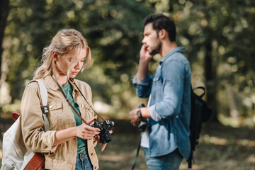 selective focus of woman with photo camera and man talking on smartphone in park