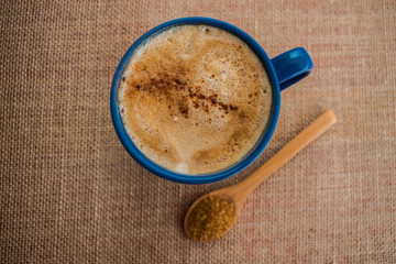 blue mug with coffee with milk and cinnamon on sack texture with sugar cane
